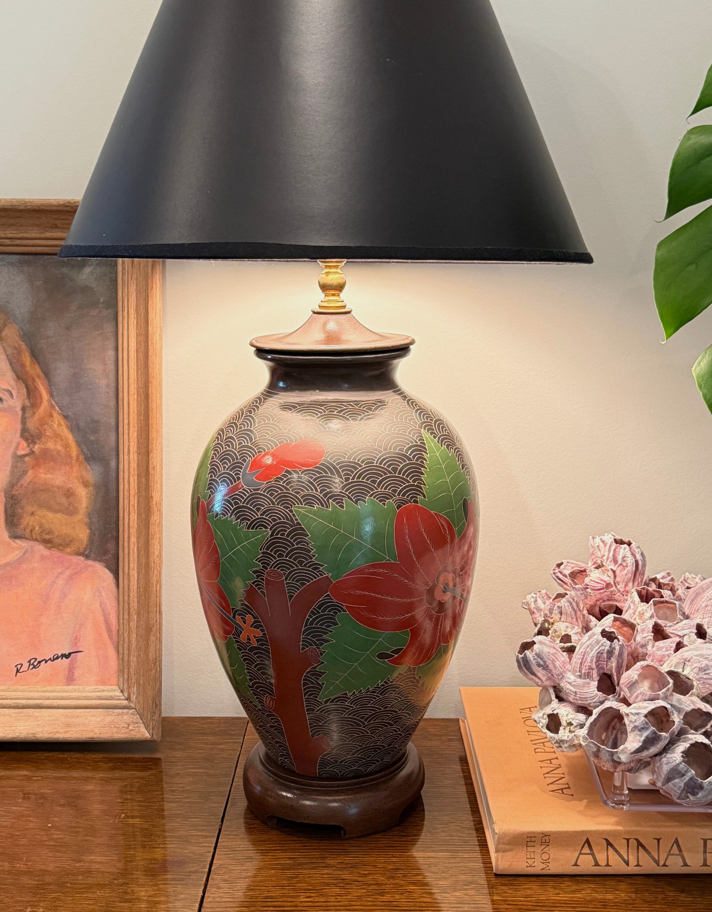 Vintage floral sgraffito lamp styled on a wooden surface with black shade, books, and art in background