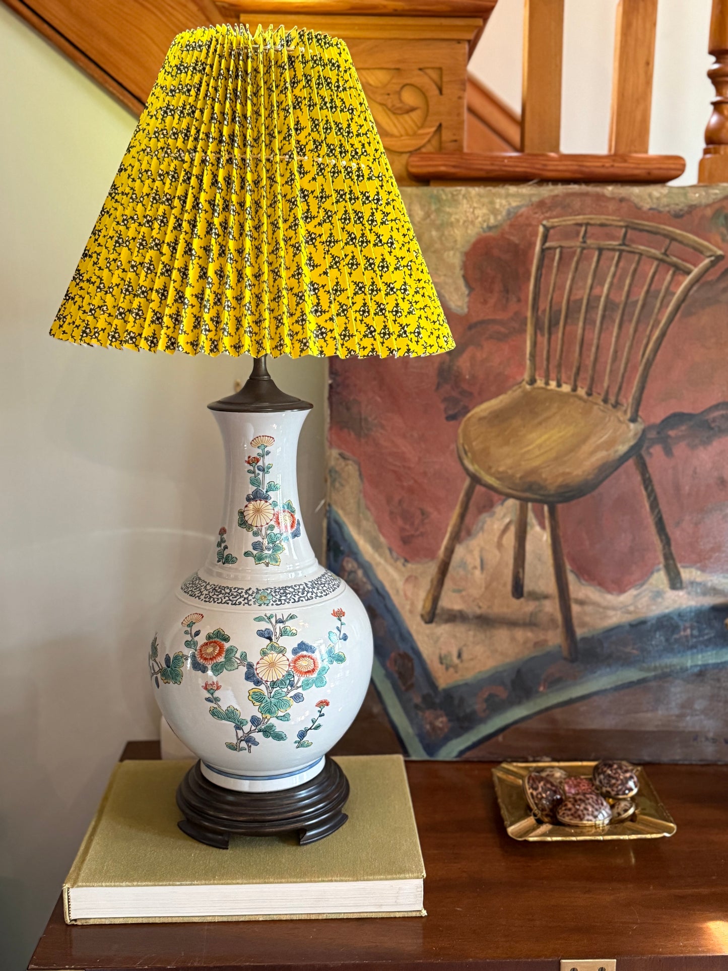 Vintage floral ceramic lamp with yellow pleated lampshade styled on console table with painting in background