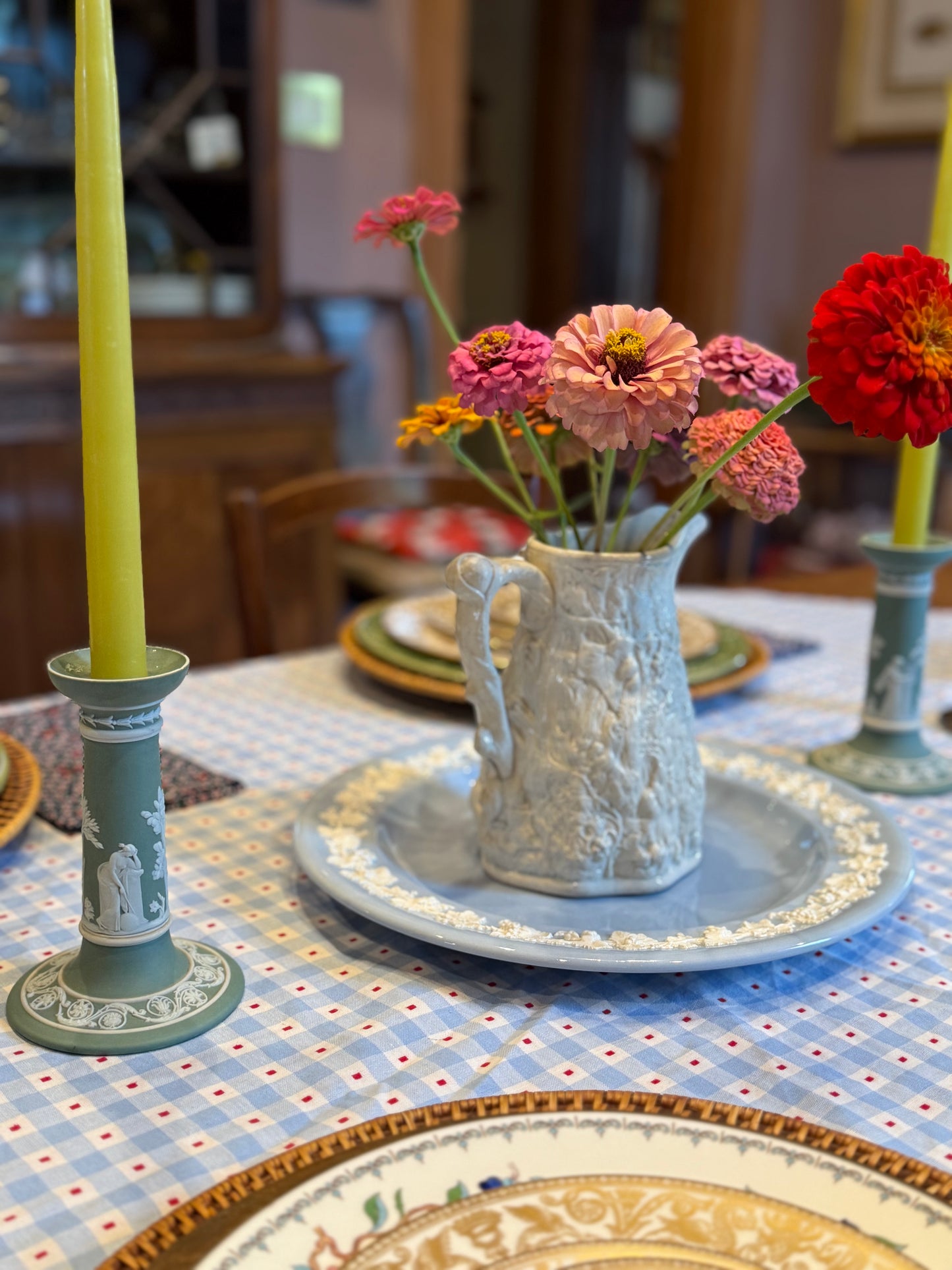Styled dining table with a pair of antique Wedgwood sage green Jasperware candlesticks featuring white neoclassical muses in relief, flanking a floral centerpiece in a textured ceramic pitcher. Candlesticks measure 6" tall and are marked “Wedgwood Made in England.”