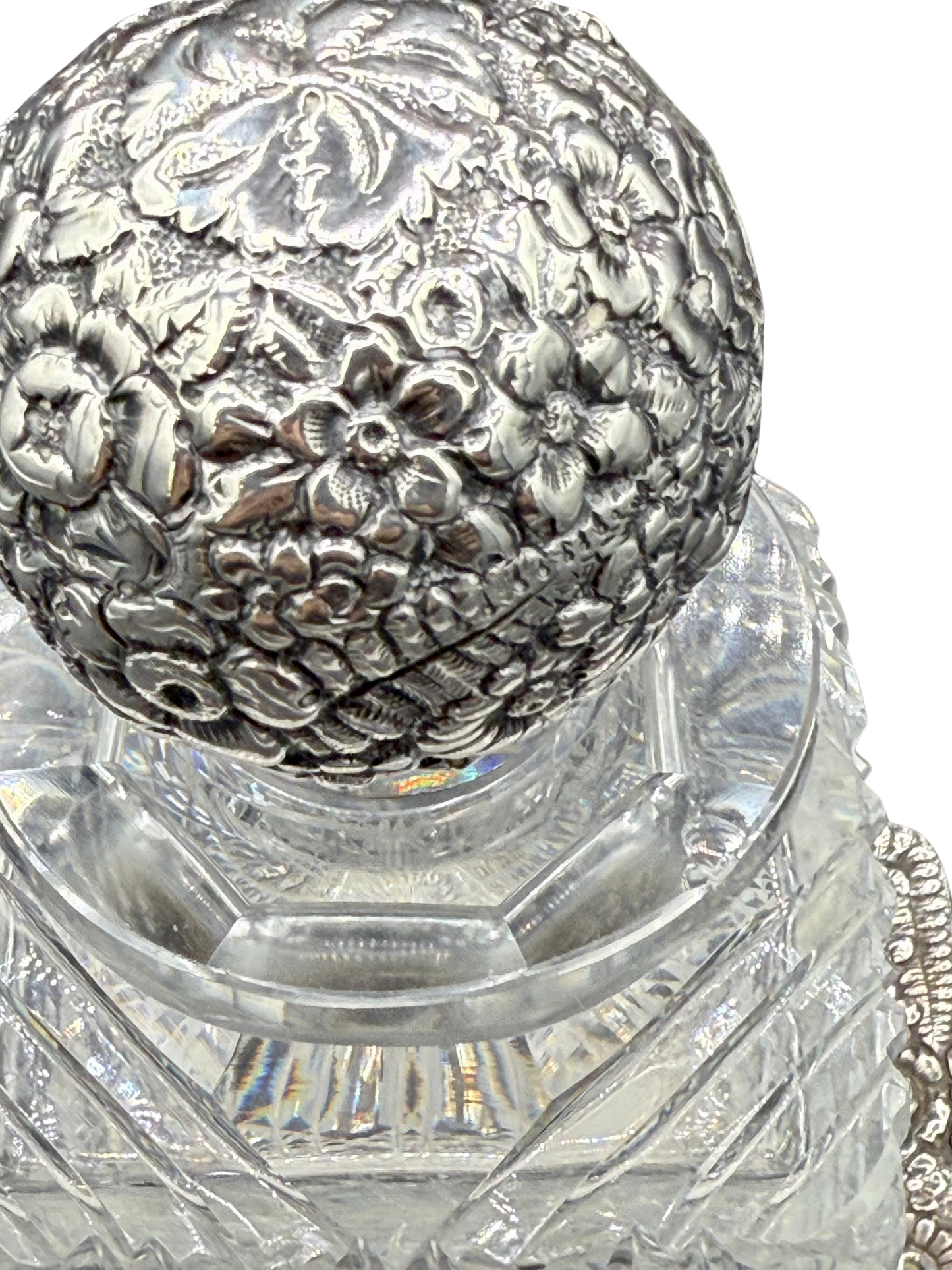 Detailed close-up of Tiffany sterling floral repoussé stopper atop antique cut crystal decanter