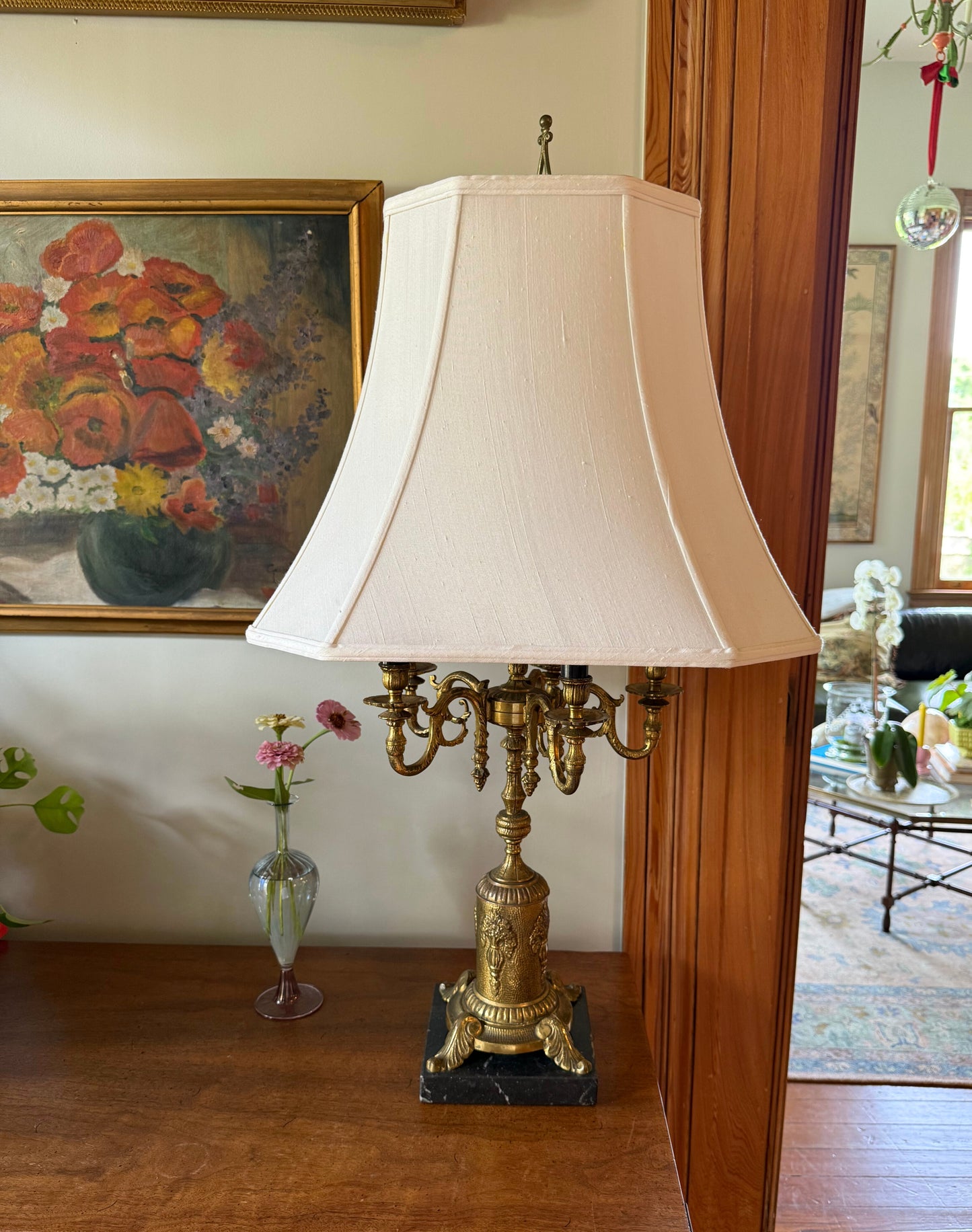 Vintage brass candelabra lamp with cream shade on wooden sideboard, styled with flowers and framed artwork in an elegant room.