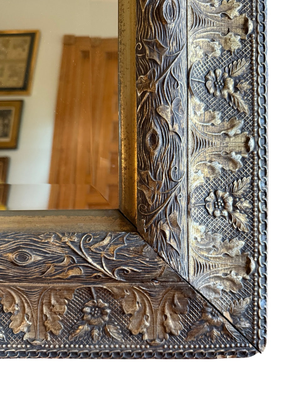 Close-up of antique silver-leaf mirror frame with detailed floral carvings and visible aged patina on carved wood”