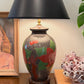 Vintage floral sgraffito lamp styled on a wooden surface with black shade, books, and art in background