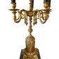 Close-up of vintage gilded brass base and scrolling candelabra arms with faux candle sleeves on a decorative table lamp.
