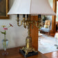 Side view of vintage neoclassical-style candelabra table lamp with six faux candle sockets and a flared fabric shade in a classic interior.