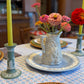 Styled dining table with a pair of antique Wedgwood sage green Jasperware candlesticks featuring white neoclassical muses in relief, flanking a floral centerpiece in a textured ceramic pitcher. Candlesticks measure 6" tall and are marked “Wedgwood Made in England.”