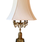 Vintage French-style candelabra table lamp with ornate brass detailing, six candle-style light sockets, and cream pagoda lampshade on black background.
