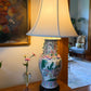 Vintage chinoiserie table lamp with fabric shade, featuring rose medallion porcelain vase, dragon imagery, and foo dog handles, styled in an interior setting.