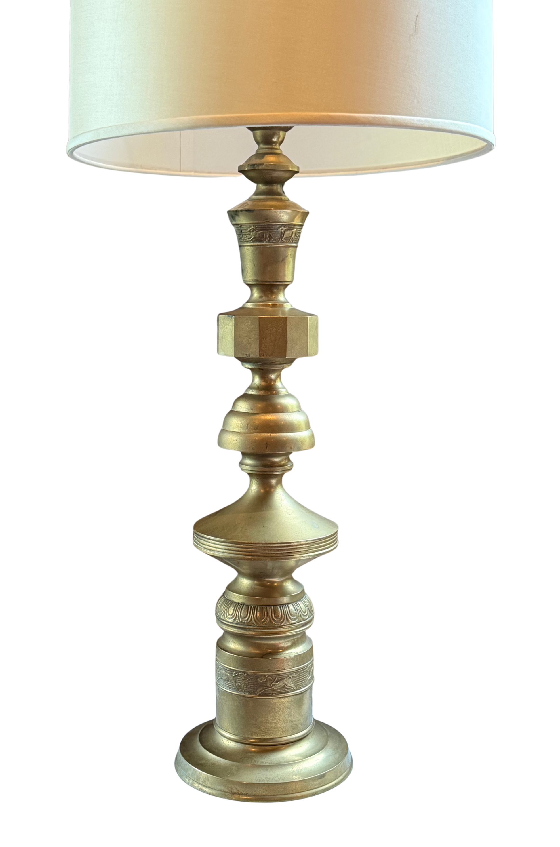 Monumental vintage brass table lamp attributed to Marbro Lamp Company, featuring sculptural stacked silhouette and low-relief animal bands, circa 1950s–60s with original patina and drum shade