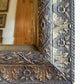Close-up of antique silver-leaf mirror frame with detailed floral carvings and visible aged patina on carved wood”