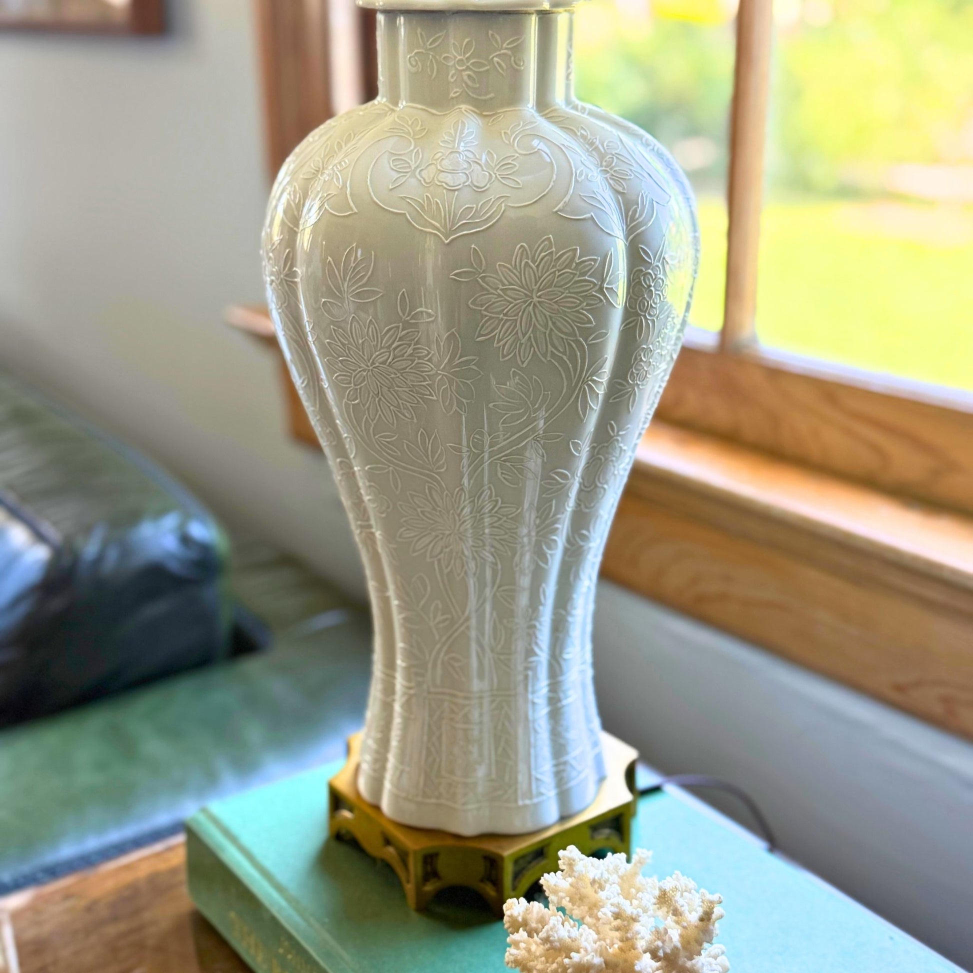 Decorative white vase with floral patterns on a green surface near a window.